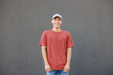 Young man wearing blank red t-shirt near gray wall. Mockup for designの写真素材