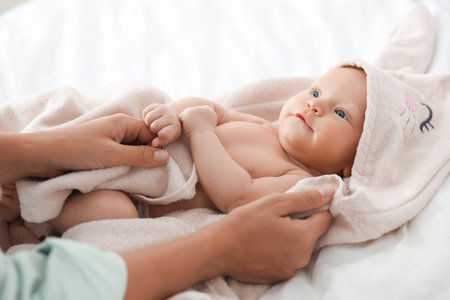 Mother covering her baby with towel after bathing on bed, closeup