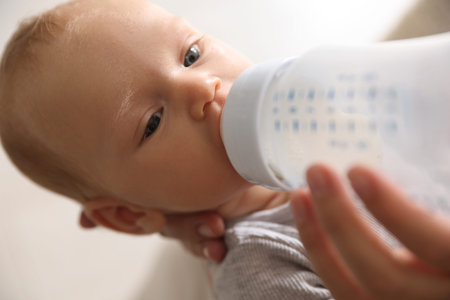 Mother feeding her little baby with bottle at home, closeup