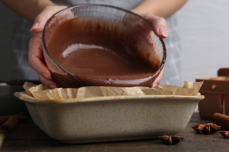 Woman pouring liquid chocolate dough into baking dish at wooden table, closeupの写真素材