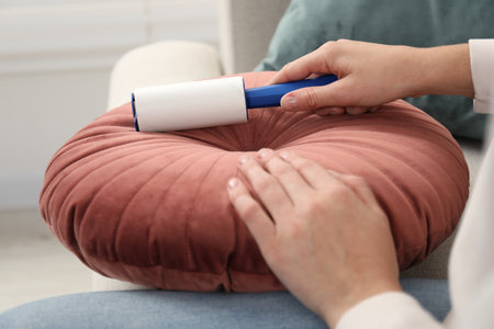 Woman cleaning cushion with lint roller at home, closeupの写真素材