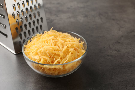 Grated cheese and grater on gray table, closeup. Space for textの写真素材