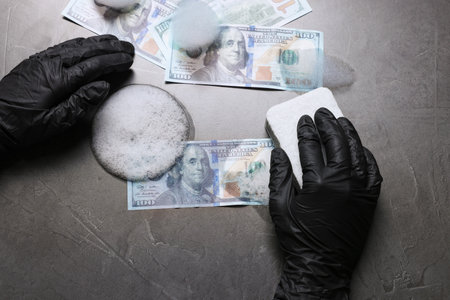 Money laundering. Man washing dollar banknotes with sponge and foam at black table, top viewの写真素材