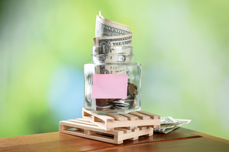 Jar with blank note and money on wooden table against blurred background, closeupの写真素材