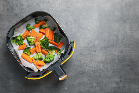 Grilled vegetables in air fryer basket on gray table, top view. Space for textの写真素材