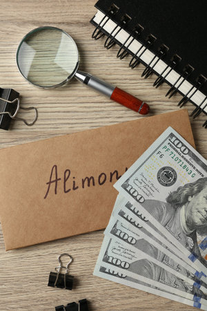 Envelope with word Alimony, money, notebook, binder clips and magnifying glass on wooden table, flat layの写真素材