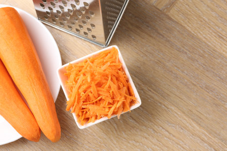 Whole and grater carrots and grater on wooden table, flat layの写真素材