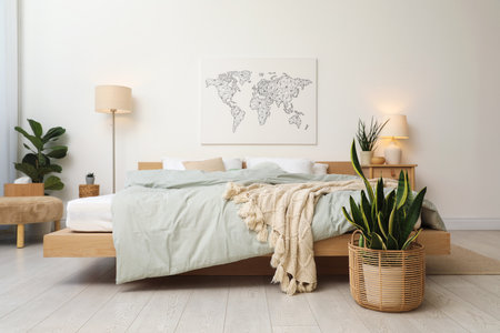 Cozy large bed with lines, furniture, houseplants and lamp near white wall in bedroom. Interior designの写真素材