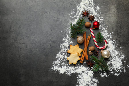 Christmas tree shape made with flour, fir branches, cookies and spices on gray table, flat lay....