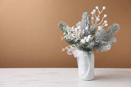Beautiful composition with fir tree branches in vase on white marble table near light brown wall indoors, space for text. Winter decorの写真素材