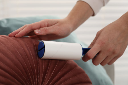 Woman cleaning cushion with lint roller at home, closeupの写真素材