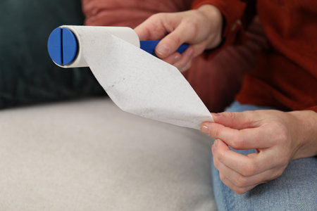 Woman removing sticky tape from lint roller at home, closeup