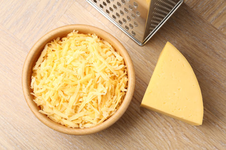 Grated and piece of cheese with grater on wooden table, flat layの写真素材