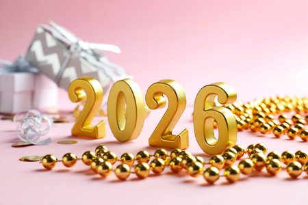New 2026 Year. Golden numbers, decorative beads, confetti and gift boxes on pink background, closeupの写真素材