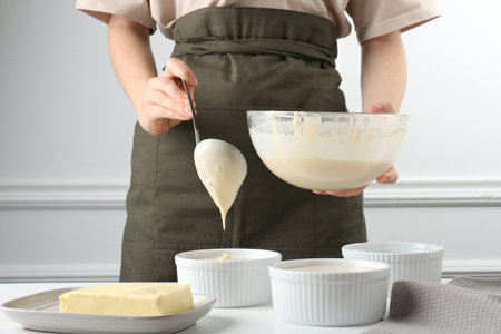 Woman pouring batter (liquid dough) into baking dishes at table indoors, closeupの写真素材