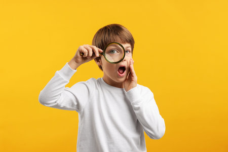Surprised little boy with magnifying glass on yellow backgroundの写真素材