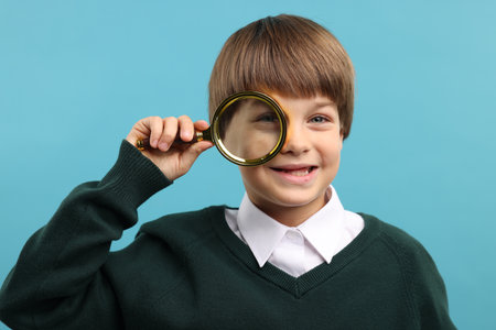Little boy with magnifying glass on light blue backgroundの写真素材