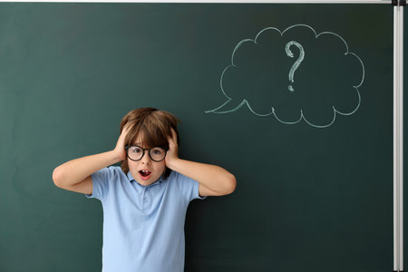 Back to school. Emotional boy near chalkboard with drawn thought bubble and question mark indoorsの写真素材
