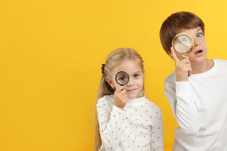 Children with magnifying glasses on yellow background. Space for textの写真素材