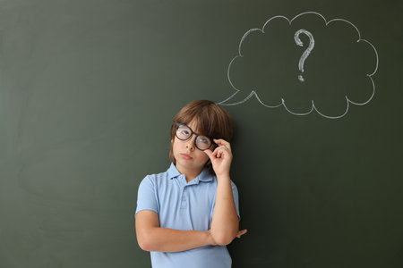 Back to school. Boy near chalkboard with drawn thought bubble and question mark indoorsの写真素材