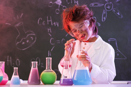 Back to school. Boy doing chemical research at desk against chalkboard with formulas indoorsの写真素材