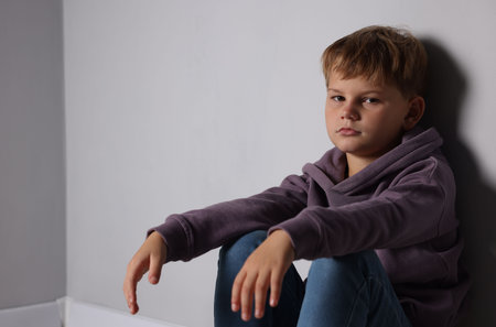 Upset little boy near light gray wall indoors, space for textの写真素材