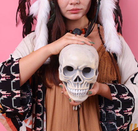 Shaman woman in native American headdress with skull on pink background, closeup