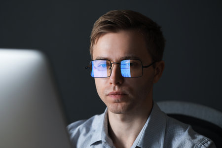 Young man wearing glasses with reflection working with computer on gray backgroundの写真素材