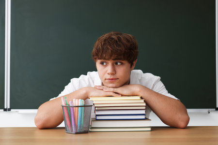 Back to school. Student with books and stationery at wooden desk against chalkboard indoorsの写真素材