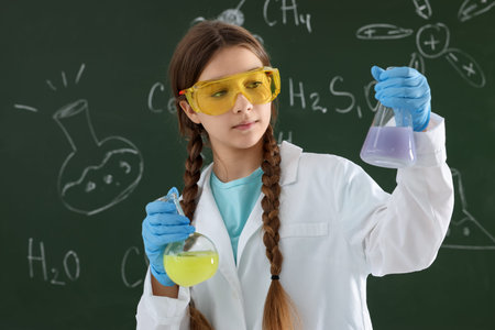 Back to school. Girl with flasks of liquids against chalkboard with chemical formulas indoors