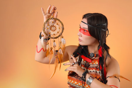 Shaman woman with face painting and dreamcatcher on pale orange gradient background, space for text