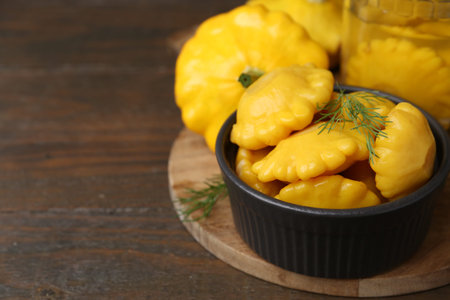 Pickled pattypan squashes with dill on wooden table, closeup. Space for text