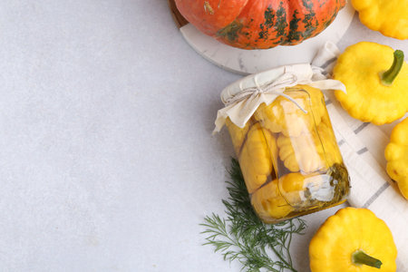 Pickled pattypan squashes in jar and fresh vegetables on light table, flat lay. Space for textの写真素材