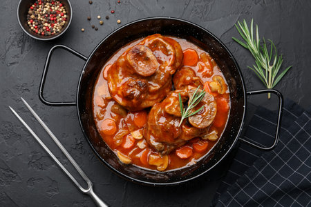 Tasty beef ossobuco with carrots and mushrooms served on dark textured table, flat layの写真素材