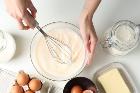 Woman making batter (liquid dough) at white table, top view