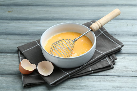 Beaten eggs in bowl and shells on wooden tableの写真素材