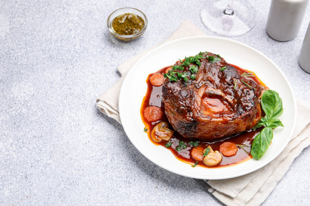 Tasty beef ossobuco with carrots, mushrooms and herbs on gray textured table, closeup. Space for textの写真素材