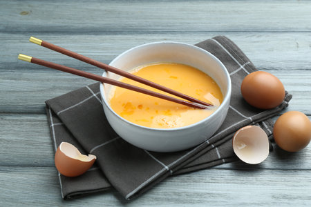 Beaten eggs in bowl and chopsticks on wooden table, closeupの写真素材