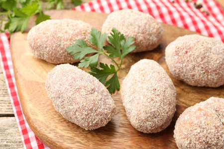 Uncooked meat patties and parsley on wooden table, closeup