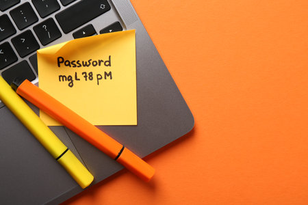 Paper note with password, markers and laptop on orange background, top view. Space for textの写真素材