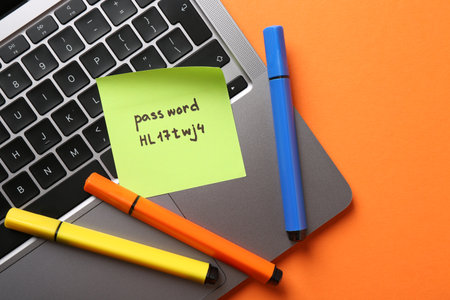 Paper note with password, markers and laptop on orange background, top viewの写真素材