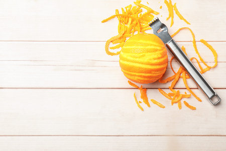 Orange zest, fresh fruit and zester tool on light wooden table, flat lay. Space for text