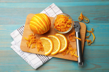 Orange zest, fresh fruits and zester tool on light blue wooden table, flat lay