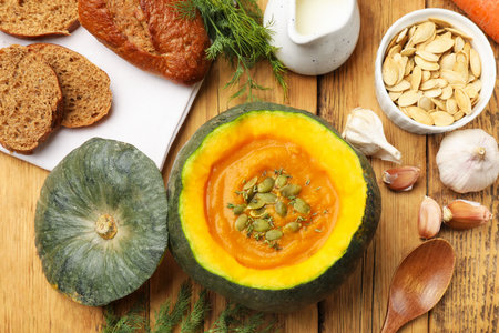 Tasty pumpkin cream soup with seeds and thyme served in pumpkin on wooden table, flat layの写真素材