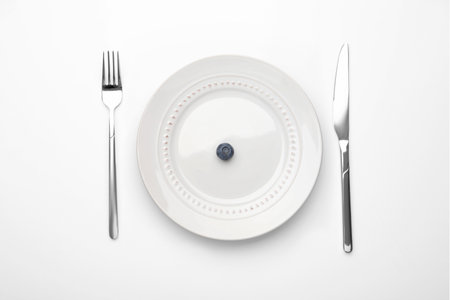 One blueberry on plate and cutlery on white table, flat layの写真素材