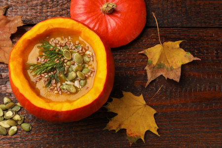 Tasty pumpkin cream soup with seeds, dill and autumn leaves on wooden table, flat layの写真素材
