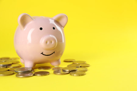 Financial savings. Piggy bank and coins on yellow background, closeup. Space for textの写真素材