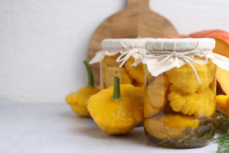 Pickled pattypan squashes in jars and fresh vegetables on light table, closeup. Space for textの写真素材