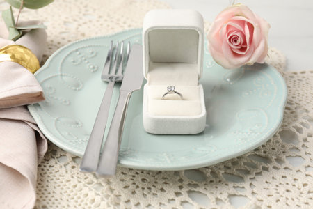Romantic place setting. Box with engagement ring, plate, cutlery, rose and napkin on white table, closeupの写真素材
