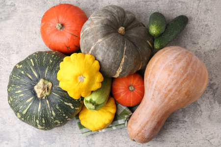 Many fresh pumpkins and other vegetables of gourd family on light gray textured table, flat lay